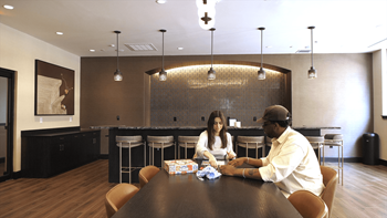 Two people sitting at a table in a room with a large painting on the wall.